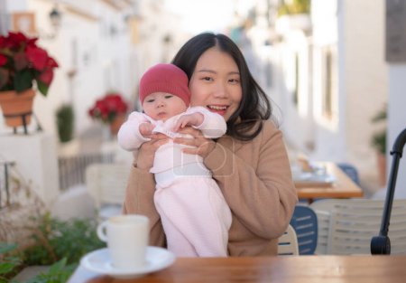 Téléchargez les photos : Jeune femme coréenne asiatique heureuse et belle tenant son adorable petite fille tout en prenant un café en plein air dans la mère fille amour et bonding concept - en image libre de droit