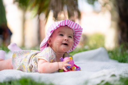 Foto de Adorable y feliz niña en sombrero de verano abraza las alegrías de la alegría en una manta suave jugando con pequeño juguete. Riéndose mientras explora las maravillas naturales de un parque al aire libre de la ciudad - Imagen libre de derechos