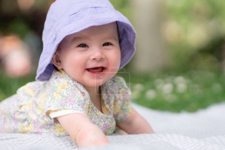 adorable and happy baby girl in summer hat embraces the joys of playfulness on a soft blanket. Laughing as she explores the natural wonders of an outdoors city park