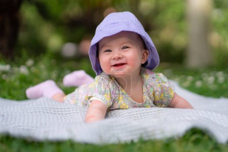 Photo for Adorable and happy baby girl in summer hat embraces the joys of playfulness on a soft blanket. Laughing as she explores the natural wonders of an outdoors city park - Royalty Free Image