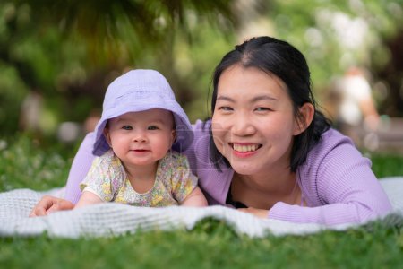 Photo for In city park a happy and adorable 5 month old baby girl and her Asian Chinese woman share a playful moment on a blanket amidst the lush green grass in love and mother daughter connection - Royalty Free Image
