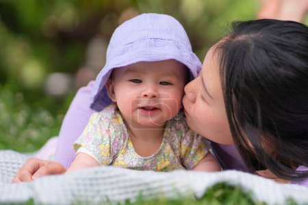 Téléchargez les photos : Dans le parc de la ville, une heureuse et adorable petite fille de 5 mois et sa femme asiatique coréenne partagent un moment ludique sur une couverture au milieu de l'herbe verte luxuriante en amour et la connexion mère-fille - en image libre de droit