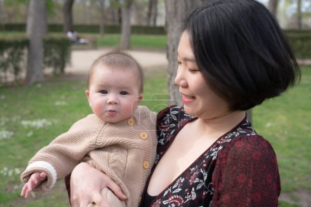 Photo for Young happy and beautiful Asian Chinese woman holding little daughter, a cute an adorable baby girl, playful together in the park in mother and child love and parenting concept - Royalty Free Image