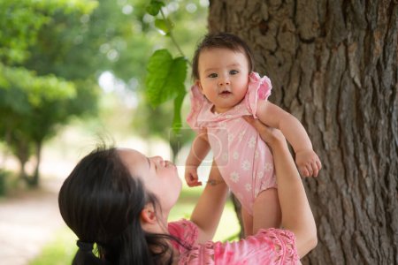 Photo for Asian mum and little child - young happy and beautiful Chinese woman playing on city park with adorable and cheerful baby girl in mother and daughter love and bonding - Royalty Free Image