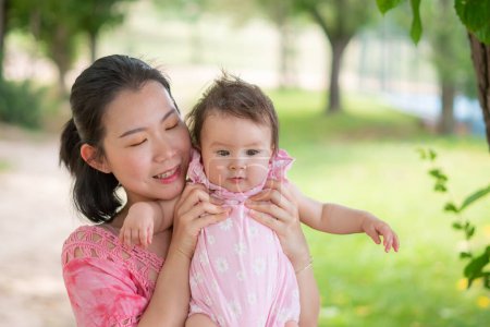 Foto de Mamá asiática y niño pequeño - joven mujer china feliz y hermosa jugando en el parque de la ciudad con adorable y alegre niña en el amor de la madre y la hija y la vinculación - Imagen libre de derechos
