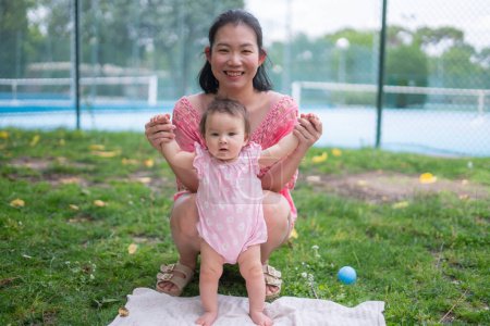 Téléchargez les photos : Maman asiatique et petit enfant - jeune femme chinoise heureuse et belle jouant sur le parc de la ville avec une adorable et joyeuse petite fille dans l'amour de la mère et de la fille et les liens - en image libre de droit