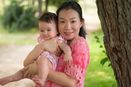 Foto de Mamá asiática y niño pequeño - joven mujer coreana feliz y hermosa jugando en el parque de la ciudad con adorable y alegre niña en el amor de la madre y la hija y la vinculación - Imagen libre de derechos