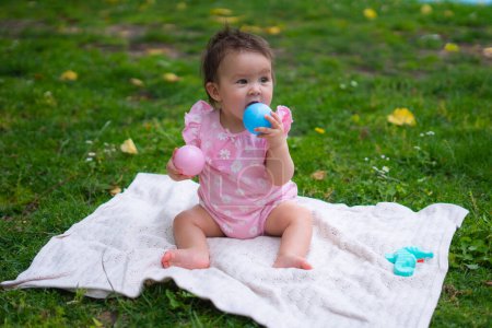 Photo for Happy and adorable 7 or 8 months old baby girl playing with ball toy cheerful sitting on towel lying on grass city park in childhood concept - Royalty Free Image