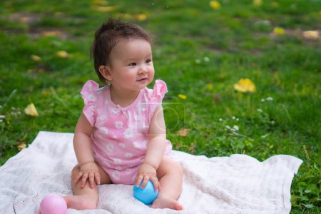 Téléchargez les photos : Heureux et adorable 7 ou 8 mois bébé fille jouer avec jouet balle joyeuse assis sur une serviette couché sur l'herbe parc de la ville dans le concept de l'enfance - en image libre de droit