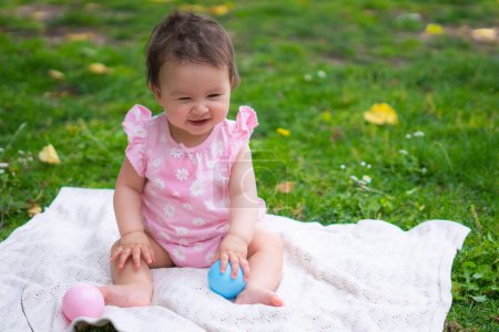 Foto de Feliz y adorable niña de 7 u 8 meses jugando con el juguete de la bola alegre sentado en la toalla acostado en el parque de la ciudad de hierba en concepto de infancia - Imagen libre de derechos