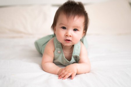 Photo for Mixed ethnicity Asian Caucasian 8 months baby girl - lifestyle home portrait of adorable and happy female child lying playful on bed exploring the surroundings curious - Royalty Free Image