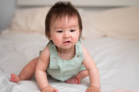 Photo for Mixed ethnicity Asian Caucasian 8 months baby girl - lifestyle home portrait of adorable and happy female child sitting playful on bed exploring the surroundings curious - Royalty Free Image
