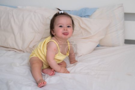 Photo for Mixed ethnicity Asian Caucasian baby girl sitting on bed - sweet and adorable little baby 8 months old with a funny pony tail looking around curious - Royalty Free Image