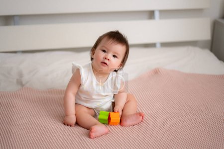Photo for Lifestyle home portrait of 9 months old mixed ethnicity Asian Caucasian baby girl playing happy and carefree on bed crawling and handling color blocks in childhood and nursery concept - Royalty Free Image