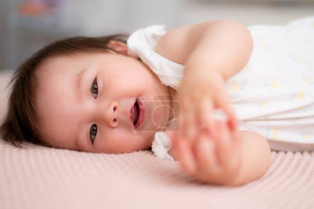 Téléchargez les photos : Mode de vie portrait à la maison de 9 mois mélange ethnique asiatique Caucasien bébé fille jouer heureux et insouciant sur lit rampant rire et excité dans l'enfance et la crèche concept - en image libre de droit