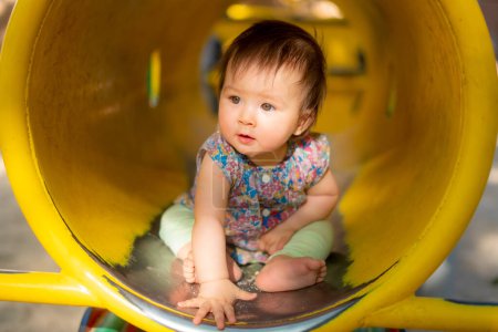 Photo for Outdoors lifestyle portrait of beautiful and adorable 9 month old baby girl sitting on yellow tube at children playground in city park exploring the surroundings cheerful and curious - Royalty Free Image