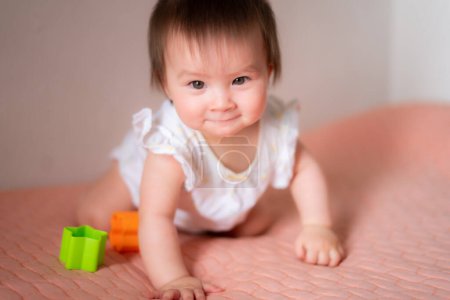Foto de Estilo de vida casa retrato de adorable y hermosa asiática caucásica mezclado bebé niña jugando en la cama con bloques de color emocionado y feliz en concepto de la infancia - Imagen libre de derechos