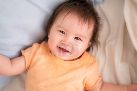Téléchargez les photos : Mode de vie portrait à la maison de heureuse et adorable fille de 9 mois regardant la caméra dans une expression drôle de visage sur fond blanc rampant sur le lit - en image libre de droit