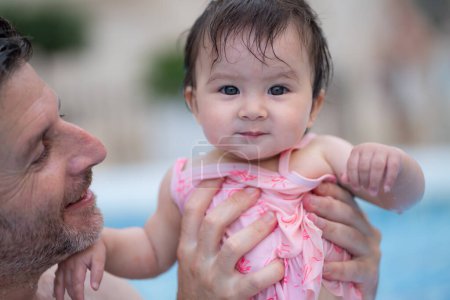 Téléchargez les photos : Portrait style de vie de père et petite fille profiter de l'été - homme tenant sa douce petite fille excitée et joyeuse jouer ensemble à la piscine de villégiature dans le concept parental - en image libre de droit