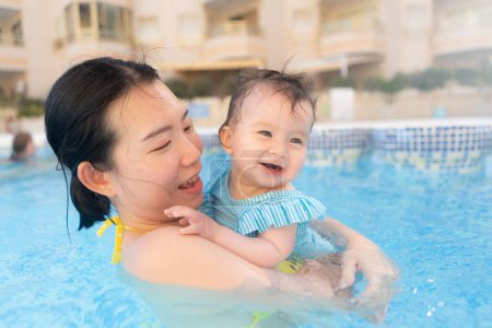 Photo for Happy and beautiful Asian woman holding her little baby girl playful - Korean mother and adorable daughter playing on water at resort swimming pool in Summer - Royalty Free Image