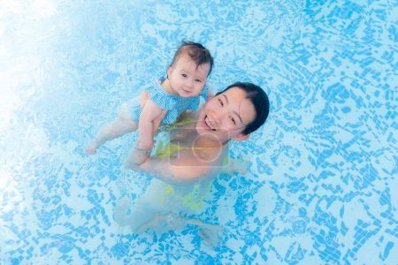 Foto de Feliz y hermosa mujer asiática sosteniendo a su pequeña niña juguetona madre coreana y adorable hija jugando en el agua en la piscina del complejo en verano - Imagen libre de derechos