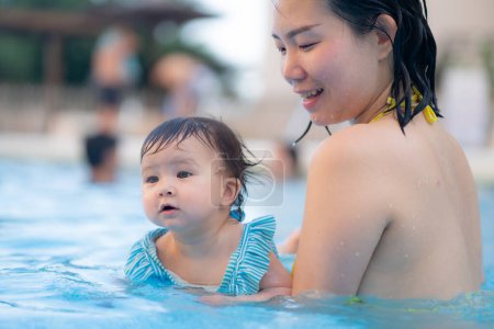 Téléchargez les photos : Heureuse et belle femme asiatique tenant sa petite fille ludique mère coréenne et adorable fille jouant sur l'eau à la piscine de villégiature en été - en image libre de droit