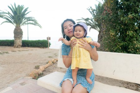 Photo for Outdoors lifestyle portrait of Asian mother and her little daughter - beautiful woman holding his adorable and happy baby girl at palm trees park enjoying Summer holidays - Royalty Free Image