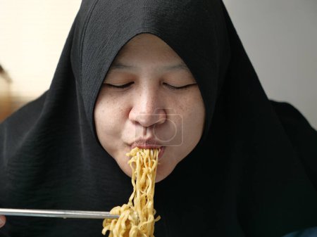 Foto de Mujer musulmana asiática comiendo fideos fritos instantáneos, comida rápida poco saludable - Imagen libre de derechos