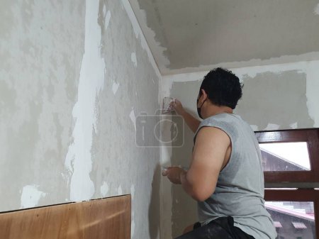 Photo for Plasterwork and wall painting preparation. Asian male applying plaster or filling drywall patch. DIY - Royalty Free Image