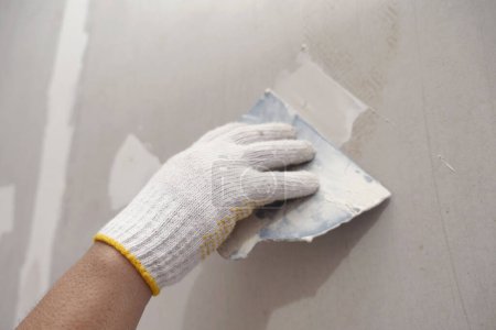 Foto de Preparación de yeso y pintura mural. cerrar la mano del artesano que aplica yeso o relleno parche de paneles de yeso - Imagen libre de derechos