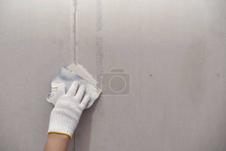 Plâtre et préparation de peinture murale. main rapprochée de l'artisan appliquant du plâtre ou remplissant le patch de cloison sèche
