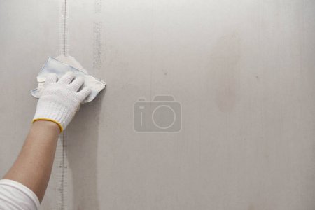 Foto de Preparación de yeso y pintura mural. cerrar la mano del artesano que aplica yeso o relleno parche de paneles de yeso - Imagen libre de derechos