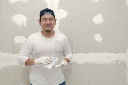 Photo for Happy Asian craftsmen smiling to camera, doing plasterwork and wall painting preparation. - Royalty Free Image