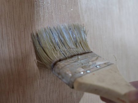 Pintor aplicando barniz claro de madera, primer movimiento del pincel