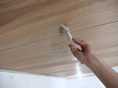 Pintor aplicando barniz claro de madera, primer movimiento del pincel