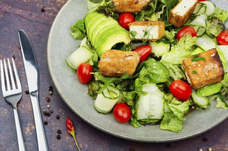 Photo for Fresh salad of greens, cucumber, avocado, tomatoes and breaded fried tofu soy cheese in a plate. Vegetarian food - Royalty Free Image