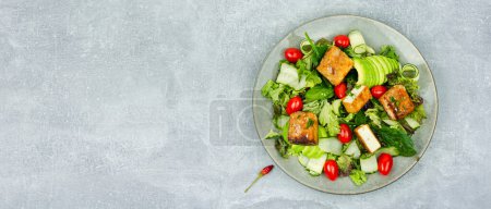 Photo for Fresh summer salad with greens, cucumber, avocado, tomatoes and breaded fried tofu soy cheese. Vegetarian food, space for text - Royalty Free Image