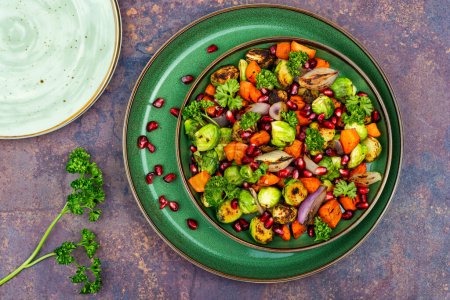Téléchargez les photos : Salad with Brussels sprouts, carrots, garnished with greens and pomegranate on a green plate - en image libre de droit