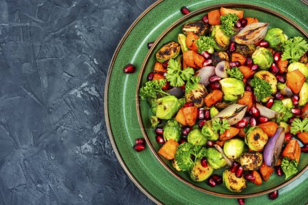Foto de Tasty salad with toasted vegetables decorated with greens and pomegranate on a green plate. Recipe place - Imagen libre de derechos