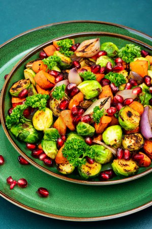 Foto de Salad with roasted Brussels sprouts, carrots, garnished with herbs and pomegranate seeds. Vegetable salad on plate - Imagen libre de derechos