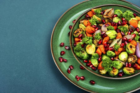 Foto de Ensalada con coles de Bruselas, zanahorias, decorada con verduras y granada en un plato verde. Espacio para texto - Imagen libre de derechos