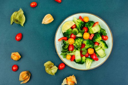 Foto de Ensalada de vitaminas con brócoli, tomate, pepino y physalis. Concepto de comida saludable, espacio para el texto - Imagen libre de derechos