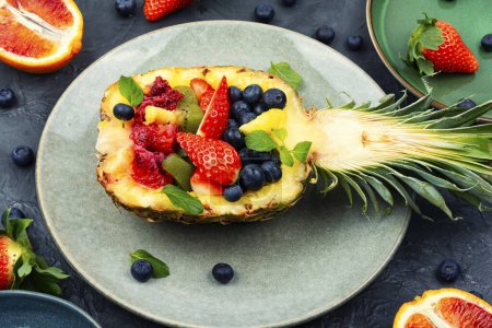 Foto de Ensalada de frutas de fresas, kiwi, bayas y naranja servida en media piña. Alimentación saludable - Imagen libre de derechos