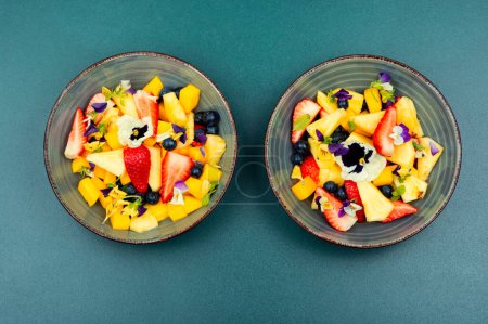Photo for Salad of pineapple, strawberries and berries, decorated with edible flowers. - Royalty Free Image