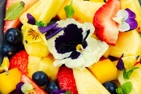 Foto de Ensalada de piña y fresas decoradas con flores comestibles, marrones de campo. Ensalada de flores con frutas. De cerca.. - Imagen libre de derechos