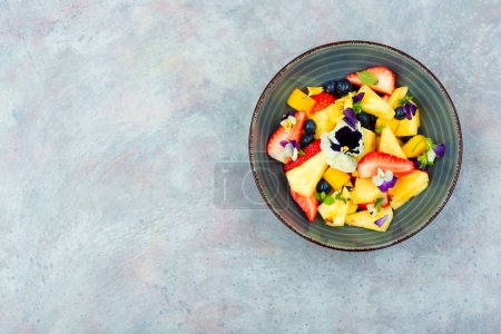 Photo for Fresh salad of pineapple, strawberries and berries, decorated with edible flowers.Copy space. - Royalty Free Image