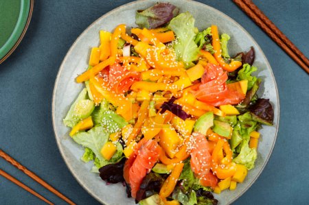 Photo for Dietary salad with smoked salmon, mango, sesame and vegetables. Salad and chopsticks - Royalty Free Image