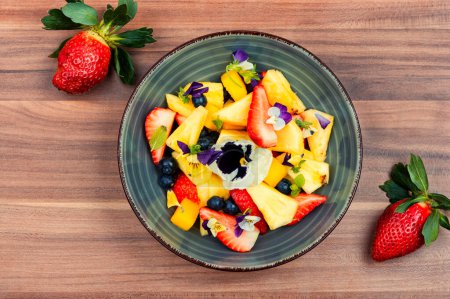 Photo for Colorful salad of pineapple, strawberries and berries, decorated with edible flowers in a bowl - Royalty Free Image
