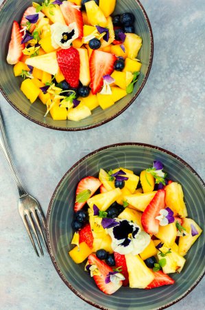 Photo for Vegan salad of pineapple, strawberries and berries, decorated with edible flowers. Top view. - Royalty Free Image