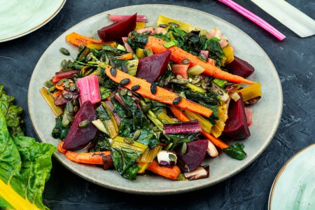 Foto de Alimento dietético - hojas de acelgas guisadas, remolachas y zanahorias. Estofado de verduras en un plato. - Imagen libre de derechos